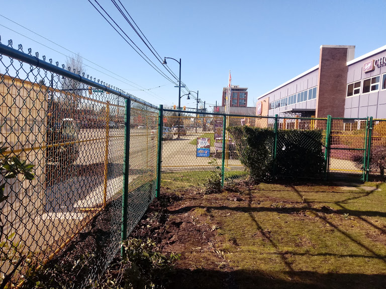 Chain link fence fitted with green privacy fabric along a commercial lot in Metro Vancouver